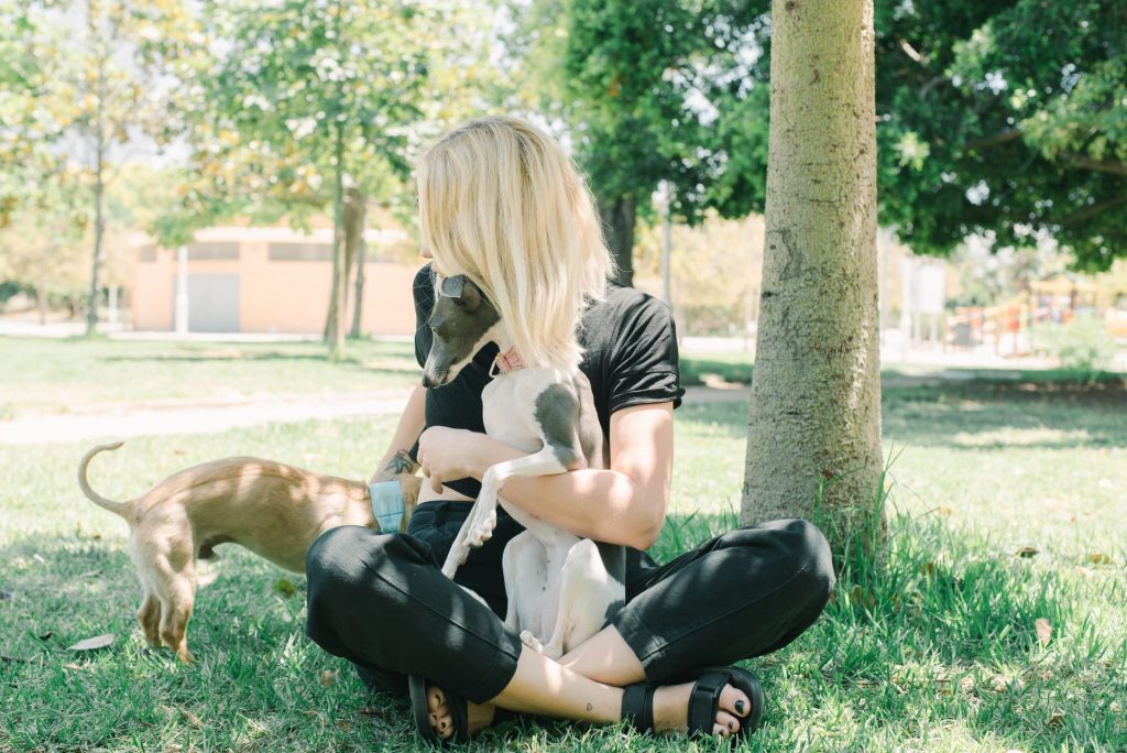 Eine blonde Frau genießt die Zeit mit Italienischen Windspielen in einem sonnigen Park.